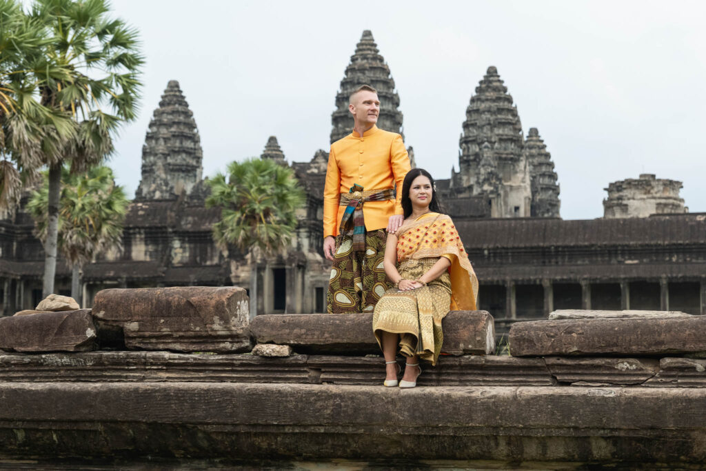 Couple in traditional Khmer wedding clothes walking through ancient Angkor Wat temple corridor during pre wedding