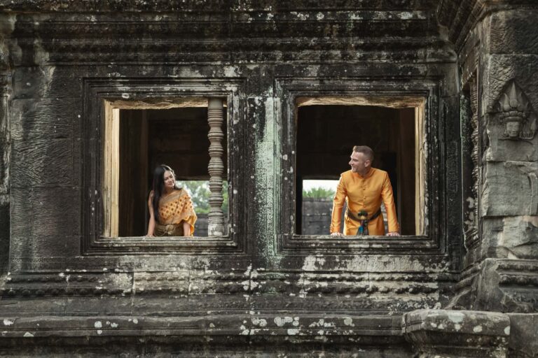 Creative Angkor Wat pre wedding photography with couple framed in ancient temple windows wearing traditional Cambodian clothing